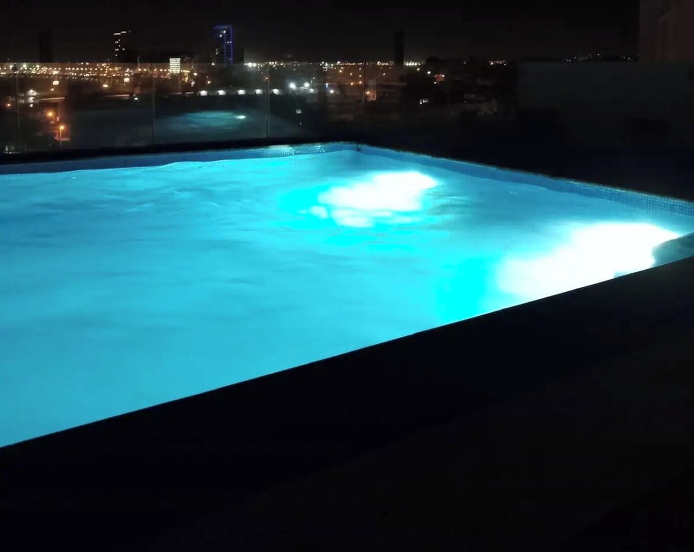 A swimming pool at night with city lights in the background.