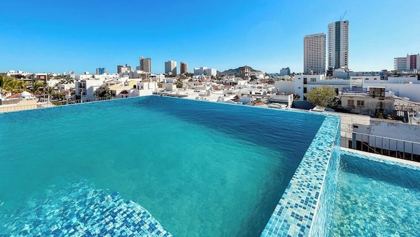 A rooftop pool with clear blue water, surrounded by white buildings and a clear sky. - Charming Apartment w/ Pool 3 Blocks to Beach (Mazatlan)