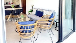 A modern living room with a sofa, two wicker chairs, a glass coffee table, and a dining area with a round table and chairs. - Charming Apartment w/ Pool 3 Blocks to Beach (Mazatlan)