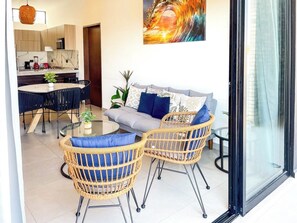 Ein modernes Wohnzimmer mit einer Couch, zwei Korbstühlen, einem Glastisch und einem Essbereich mit rundem Tisch und Stühlen.