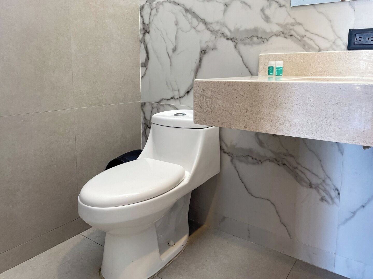 A modern bathroom with a toilet, marble walls, and a countertop with toiletries.