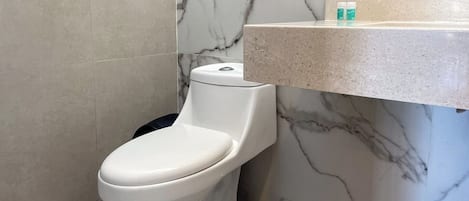 A modern bathroom with a toilet, marble walls, and a countertop with toiletries.