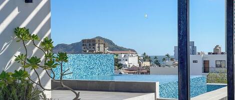 A rooftop pool with a clear view of the sea and buildings in the background.
