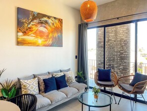 Ein modernes Wohnzimmer mit einer Couch, zwei Korbstühlen, einem Glastisch und einem großen Gemälde einer Welle.
