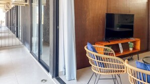 A modern hotel room with a flat-screen TV, wicker chairs, a small table, and a large window with curtains. - Charming Apartment w/ Pool 3 Blocks to Beach (Mazatlan)