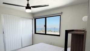Una camera da letto con un letto, una finestra vista, una ventola a soffitto e un comodino in legno.