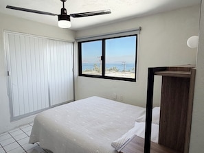 Ein Schlafzimmer mit einem Bett, einem Fenster mit Ausblick, einem Deckenventilator und einem Nachttisch aus Holz.