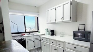 Una cucina con mobili bianchi, un piano cottura, un forno a microonde e una finestra con vista.