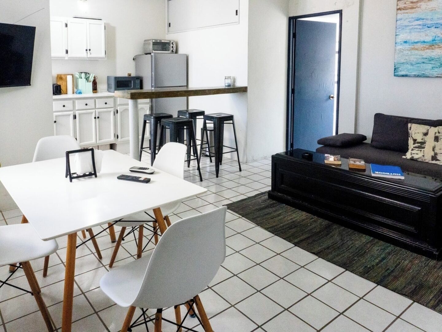 Un espace de vie compact comprenant une table à manger, des chaises, un canapé, une table basse, un coin cuisine équipé d’appareils électroménagers et une porte.