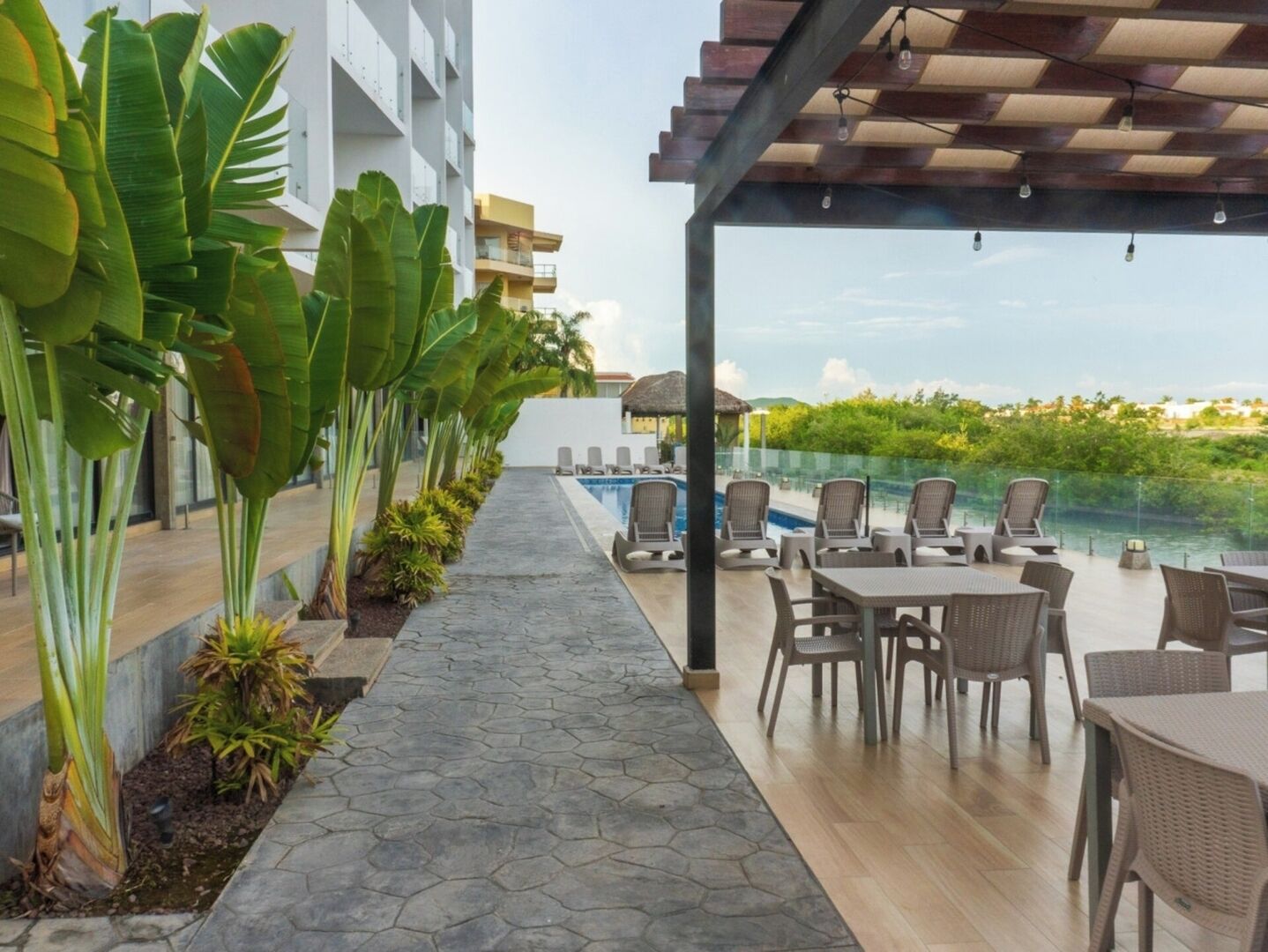 A poolside area with lounge chairs and tables, a stone pathway, and large banana plants.