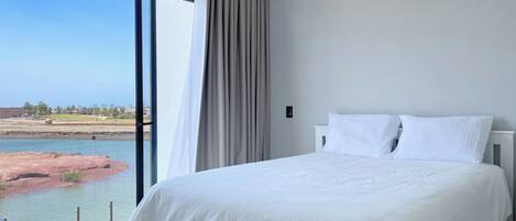 A hotel room with a large bed, a view of a body of water, and a curtain.