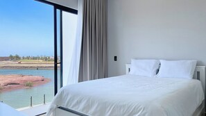 Una camera d'albergo con un letto grande, vista su un corpo d'acqua e una tenda.