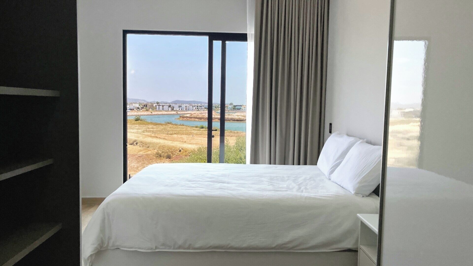 Ein Schlafzimmer mit großem Fenster, einem Bett und Blick auf eine Landschaft.