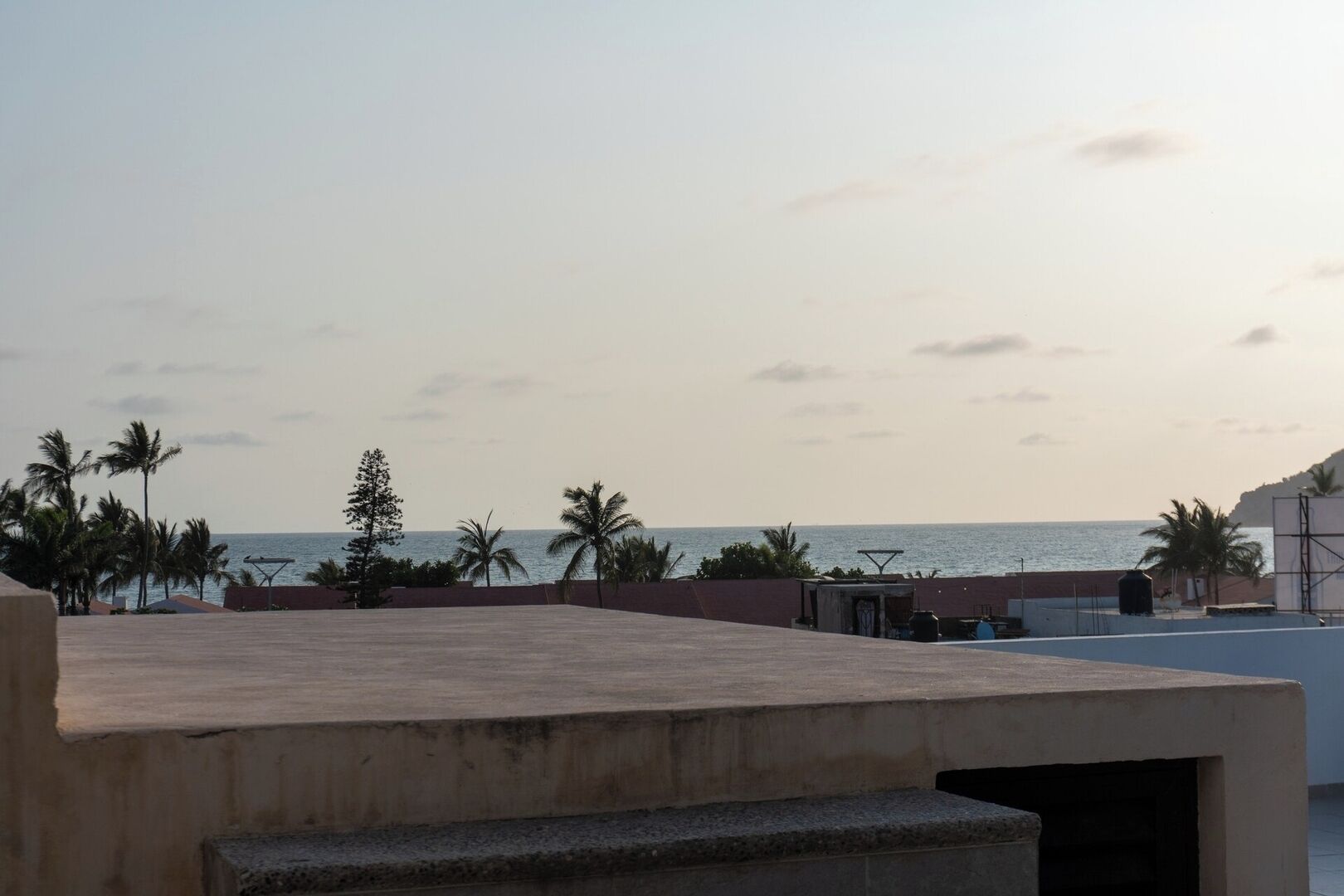 Une terrasse sur le toit offrant une vue sur la mer, les palmiers et un ciel dégagé.