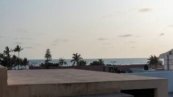 Une terrasse sur le toit offrant une vue sur la mer, les palmiers et un ciel dégagé.