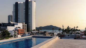 Ein Pool auf dem Dach mit Blick auf einen Berg und einen Strand, umgeben von Gebäuden.