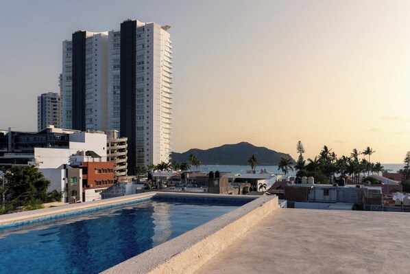 A rooftop pool with a view of a mountain and a beach, surrounded by buildings. - Cozy apartment just two blocks from the beach (Mazatlan)