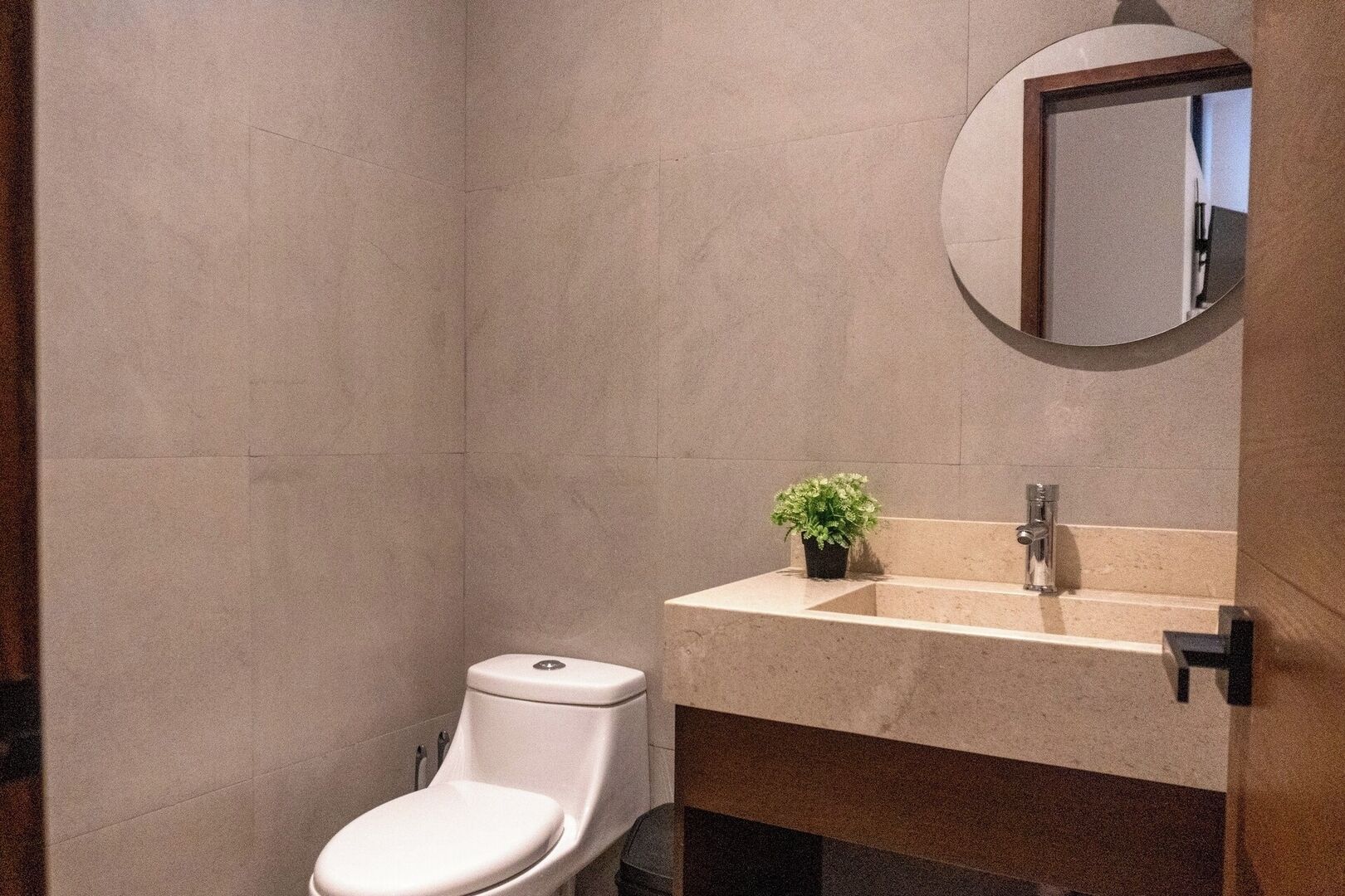 Ein Badezimmer mit Toilette, Waschbecken, Spiegel und einer kleinen Topfpflanze.