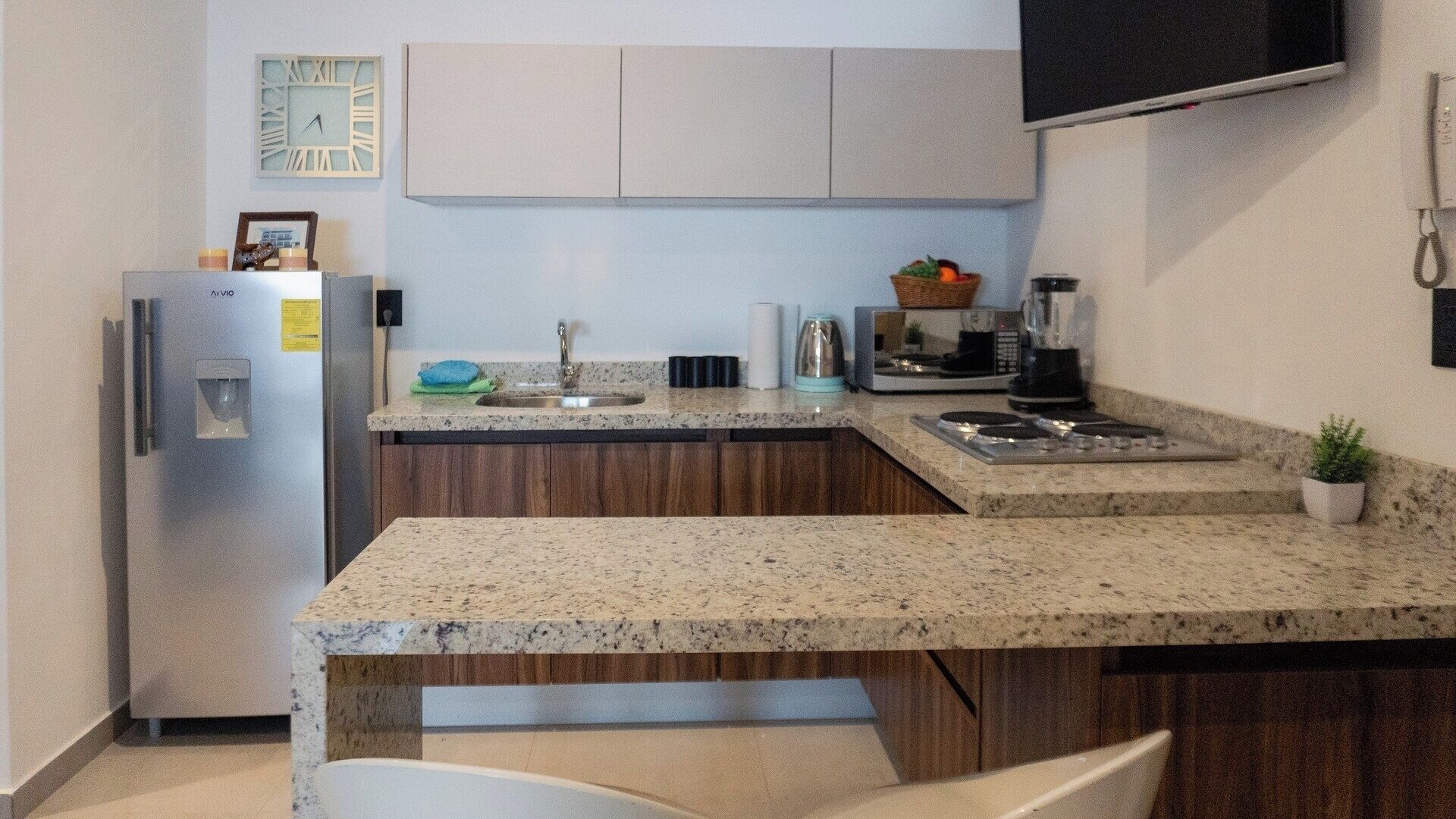 Una cocina con refrigerador, pileta, cocina y un televisor de pantalla plana montado en la pared.