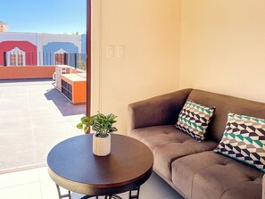 Ein Zimmer mit einer Couch, einem kleinen Tisch mit einer Pflanze und Blick auf ein Gebäude.