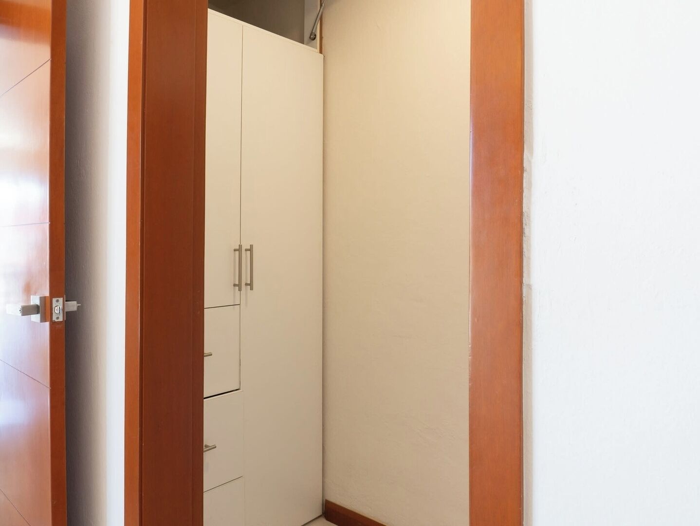 Un pasillo estrecho con un marco de puerta de madera y un armario blanco con dos puertas y un cajón.
