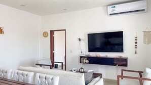 A modern living room with a sofa, a coffee table, a TV mounted on the wall, and an air conditioning unit. - Beautiful apartment 3 blocks from the beach (Mazatlan)