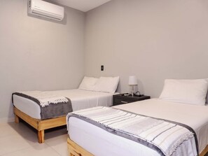 Ein Zimmer mit zwei Einzelbetten, einem Nachttisch mit Lampe und einer Wandgerätet Klimaanlage.