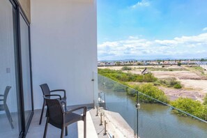 Ein Balkon mit zwei Stühlen, einem Glasgeländer und Blick auf einen Fluss sowie entfernte Gebäude.