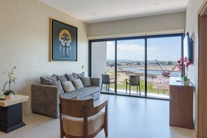 Ein modernes Wohnzimmer mit Sofa, Sesseln, einem Couchtisch und einem großen Fenster mit Blick auf ein Gewässer und Gebäude in der Ferne.