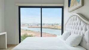 Une chambre avec une grande fenêtre, un lit et un tableau accroché au mur.