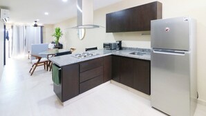 Eine moderne Küche mit dunklen Schränken, einem Edelstahlkühlschrank, einem Einbauofen und einer Kaffeemaschine.