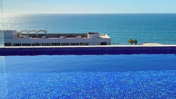Ein Pool mit blauen Fliesen, ein Gebäude mit weißer Fassade und Meerblick.