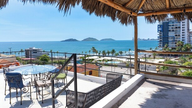 Un balcón con vista al mar, una piscina y un edificio al fondo.