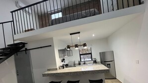 Una cocina moderna con una isla central, taburetes de bar, un refrigerador de acero inoxidable y una escalera que sube a un nivel superior.
