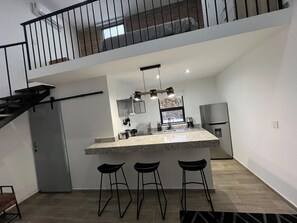 Una cucina moderna con isola centrale, sgabelli da bar, un frigorifero e una scala che conduce a un piano superiore.