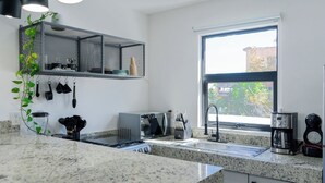 Cocina moderna con encimera de granito, cafetera, lavamanos y ventana con vistas a edificios.