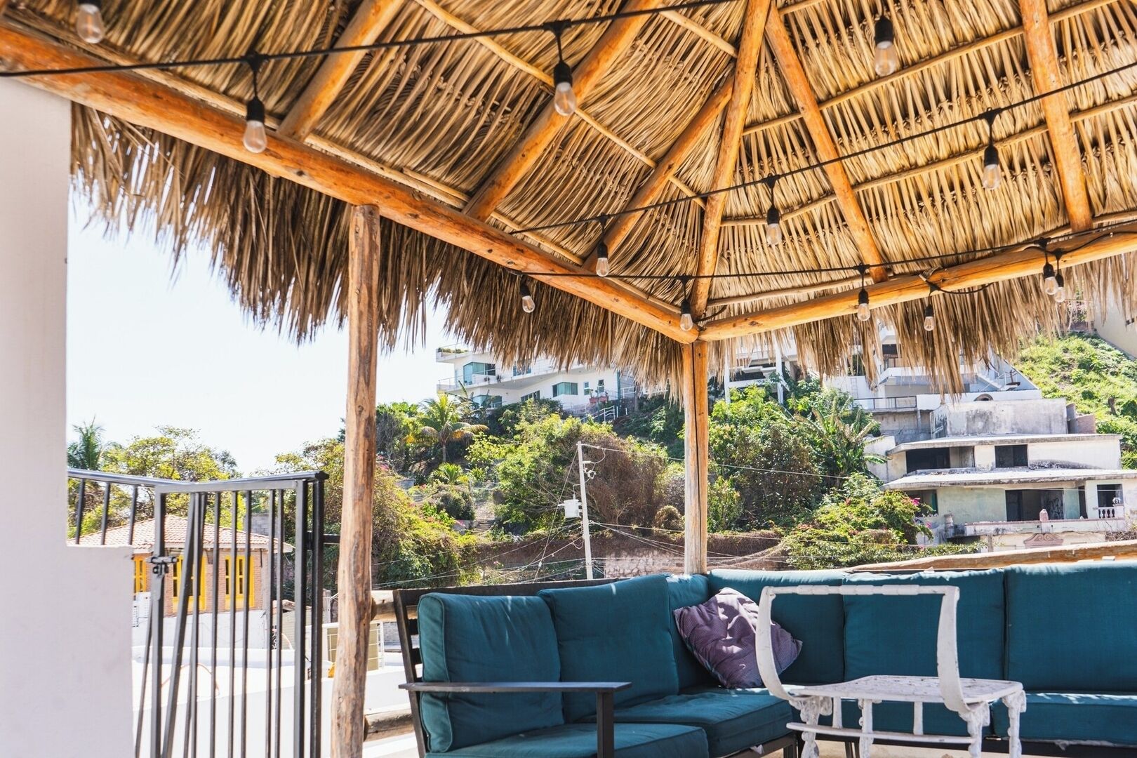 A covered outdoor seating area with a thatched roof, a green sofa, and a small table.