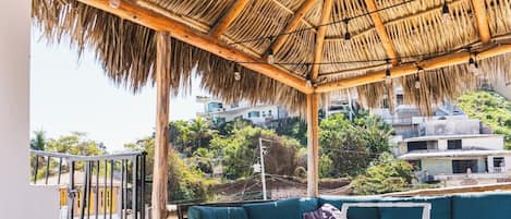 A covered outdoor seating area with a thatched roof, a green sofa, and a small table.