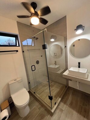 Un bagno moderno con doccia vetrata, un water, un lavandino con specchio e una ventola a soffitto.