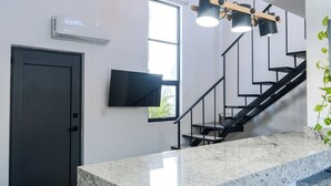 Una cocina moderna con encimera de granito, una escalera negra, un televisor de pantalla plana y una ventana con vistas a zonas verdes.