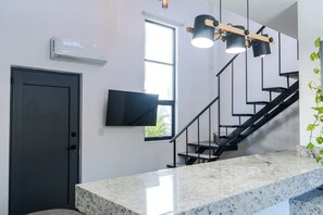 Una cucina moderna con un piano di lavoro in granito, una TV a schermo piatto, una scala e una porta nera.