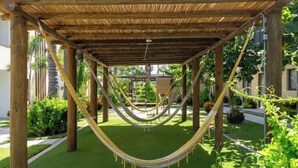 Una hamaca bajo una pérgola de madera en un jardín con vista a un edificio al fondo.
