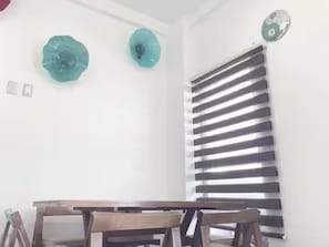 Ein Essbereich mit Tisch und Stühlen, ein Fenster mit horizontalen Rollläden und zwei dekorative Wandelemente.