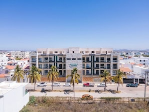 Ein mehrstöckiges Hotel mit modernem Design, das Balkone und einen Parkplatz mit mehreren Autos bietet.