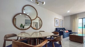 Ein modernes Wohnzimmer mit einem runden Glastisch, Holzstühlen, einem blauen Sofa und einer Deckenleuchte.