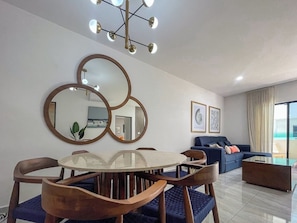 Una sala moderna con una mesa redonda de vidrio, sillas de madera, un sofá azul y un lámpara colgante.