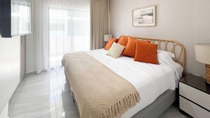 Ein Hotelzimmer mit Bett, Fernseher, Nachttisch, Lampe und einem Fenster mit Vorhängen.