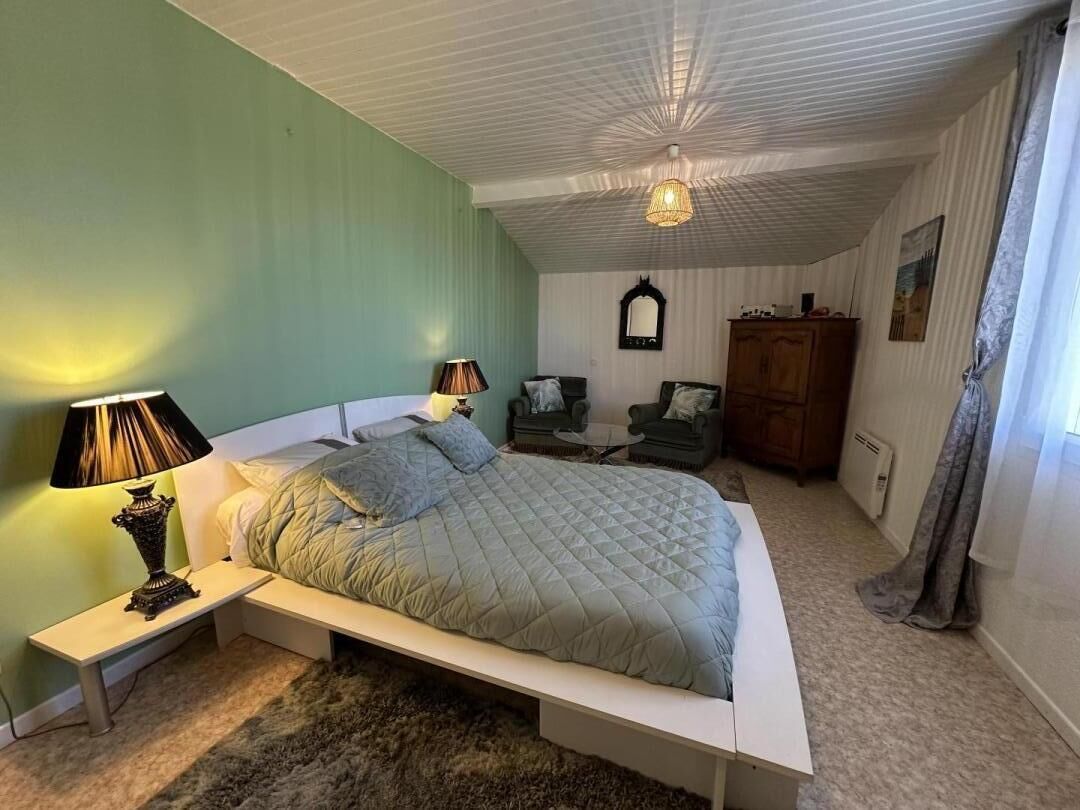 Un dormitorio con cama, lámparas de noche, una mesita, una silla, un espejo y un armario.