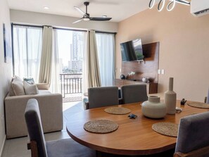Ein modernes Wohnzimmer mit einem runden Holzesstisch, grauen Sofas und einem an der Wand befestigten Fernseher.