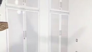 Een kamer met twee witte kasten, een bed met een witte spreideken en een houten hoofdeinde.